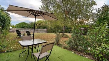 An outdoor patio area with a table and chairs, a large umbrella, and a grassy lawn.