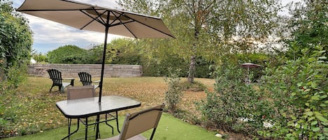 An outdoor patio area with a table and chairs, a large umbrella, and a grassy lawn.