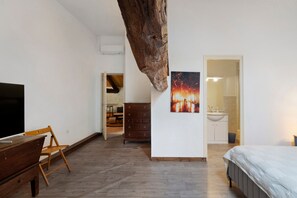 A room with a wooden floor, a bed, a dresser, a television, and a painting. - Room 'Chambre B' with Shared Pool, Wi-Fi and Air Conditioning (Ribérac)