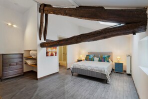 A bedroom with a large wooden beam ceiling, a bed with patterned pillows, a dresser, and a nightstand with a lamp. - Room 'Chambre B' with Shared Pool, Wi-Fi and Air Conditioning (Ribérac)