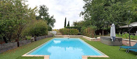 A rectangular swimming pool with a surrounding grassy area, a hot tub, and a covered seating area.