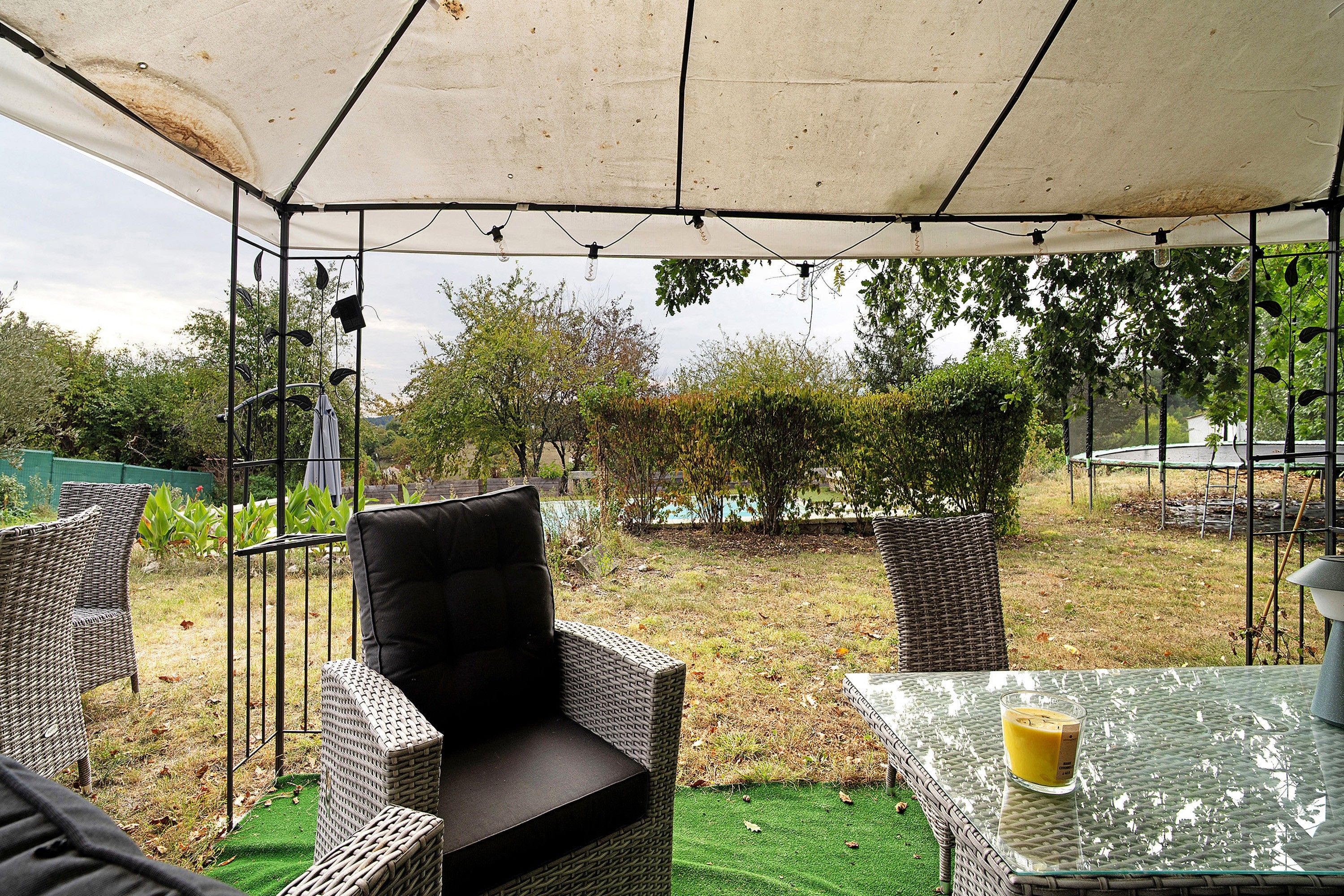 Un área de estar al aire libre con sillas de mimbre y una mesa, bajo un toldo.