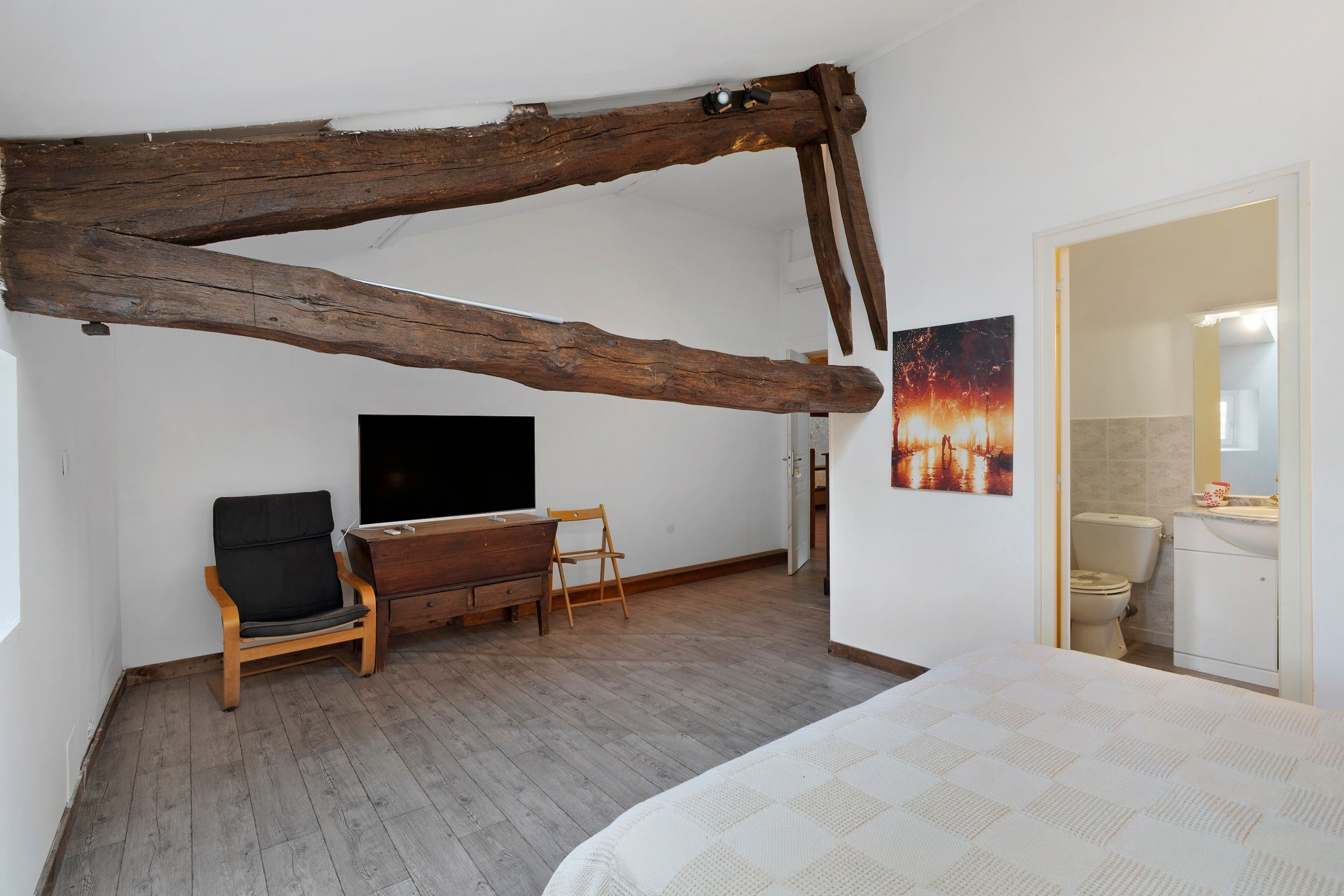 Une chambre avec une poutre en bois au plafond, un lit, une télévision, un bureau et une chaise.