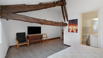 Ein Schlafzimmer mit Holzbalken, einem Bett, einem Fernseher, einem Schreibtisch und einem Stuhl.