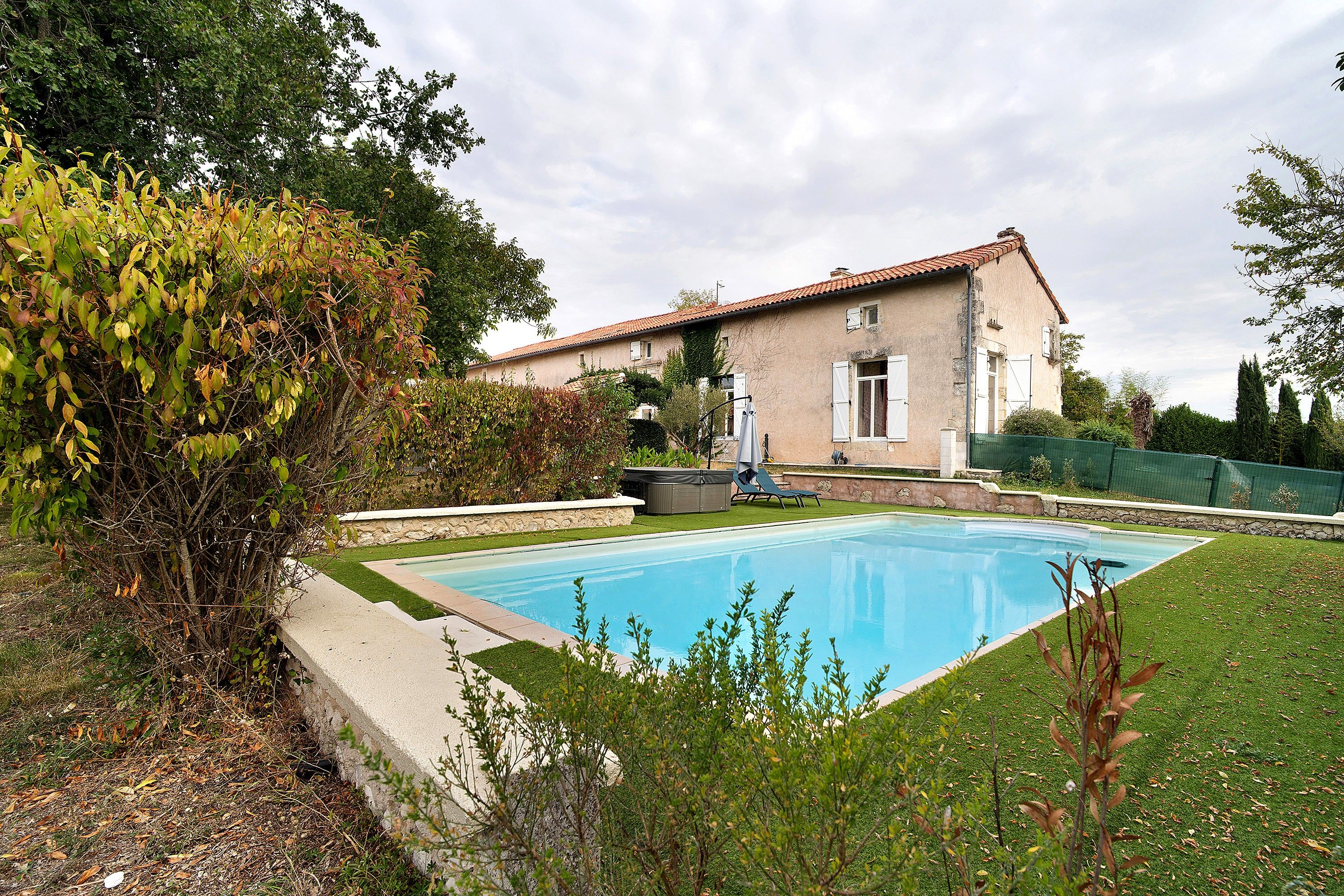 Ein Haus mit Swimmingpool, umgeben von viel Grün und einer Steinmauer.