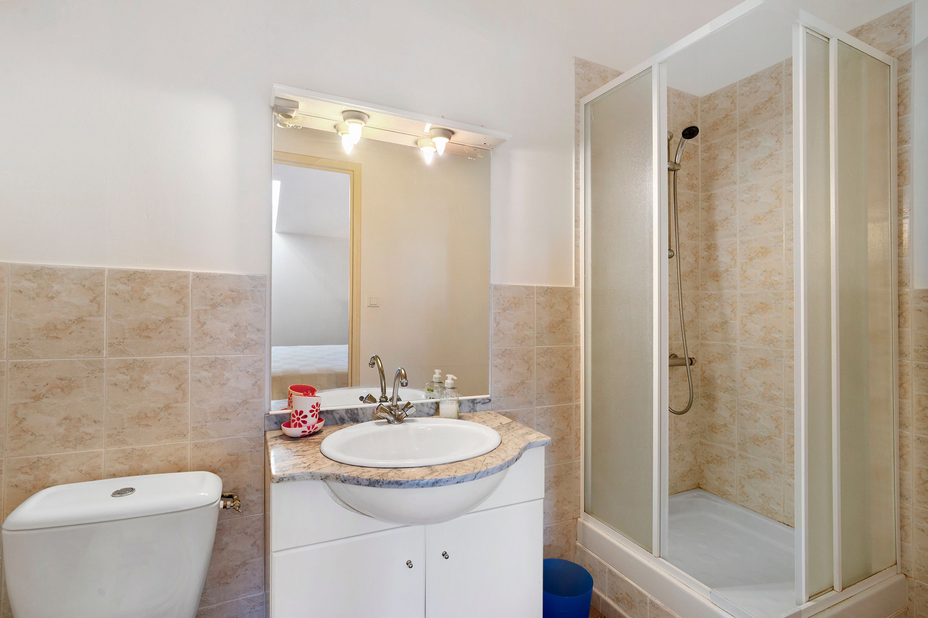 Ein Badezimmer mit einer weißen Toilette, einem Waschbecken mit Marmorplatte, einem Spiegel und einer Duschkabine.