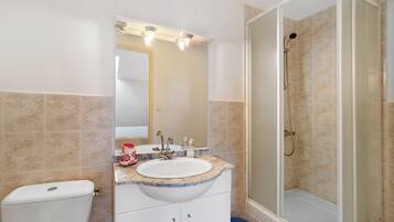 Ein Badezimmer mit einer weißen Toilette, einem Waschbecken mit Marmorplatte, einem Spiegel und einer Duschkabine.