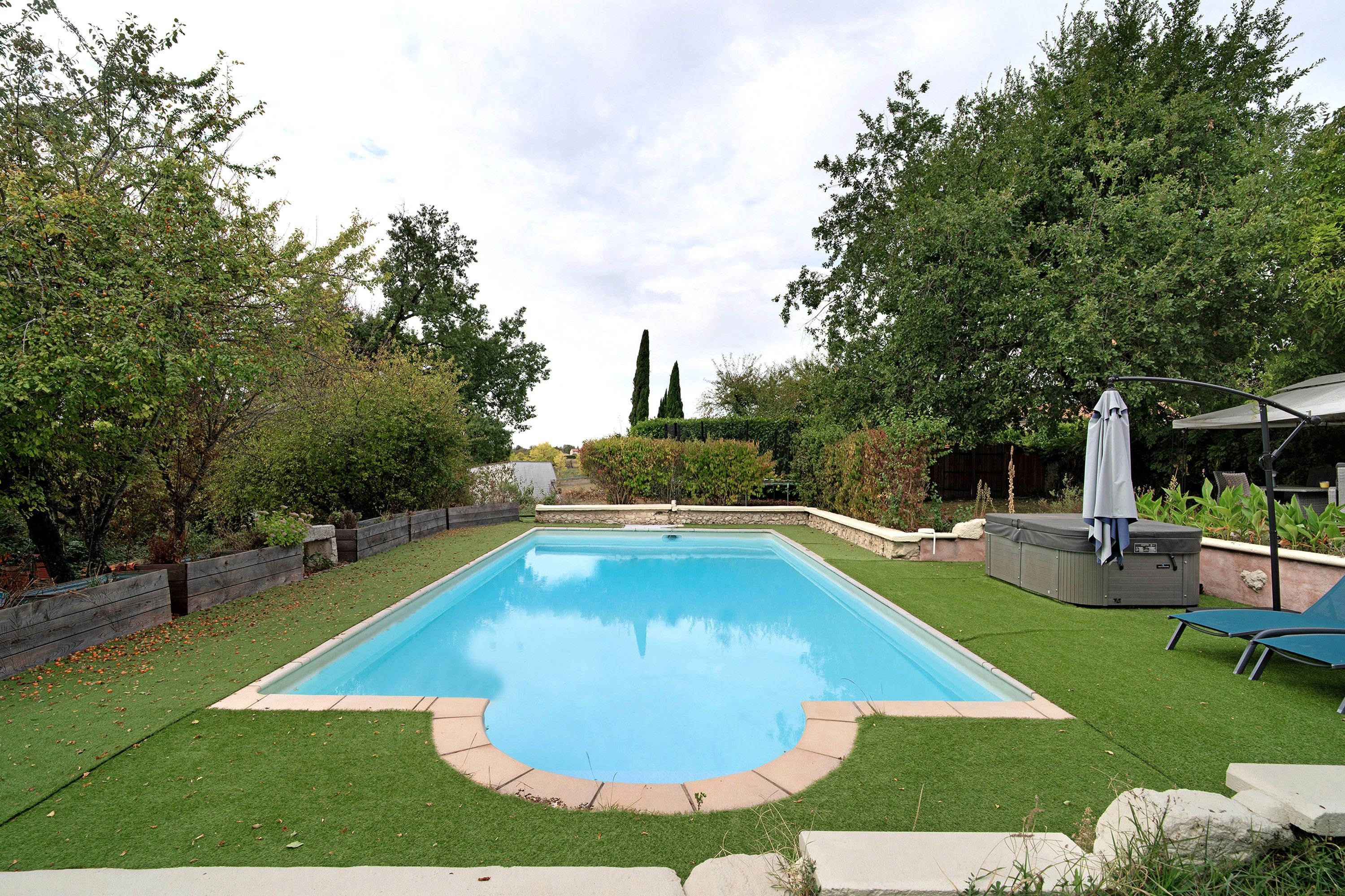 Une piscine rectangulaire entourée d’une pelouse, avec un jacuzzi et un espace salon couvert.