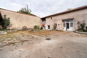A rustic building with a stone wall, a gravel courtyard, and a traditional door. - Guest House 'Chambre C' with Shared Pool, Wi-Fi and Air Conditioning (Ribérac)