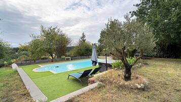 A backyard with a swimming pool, two lounge chairs, and a hot tub.