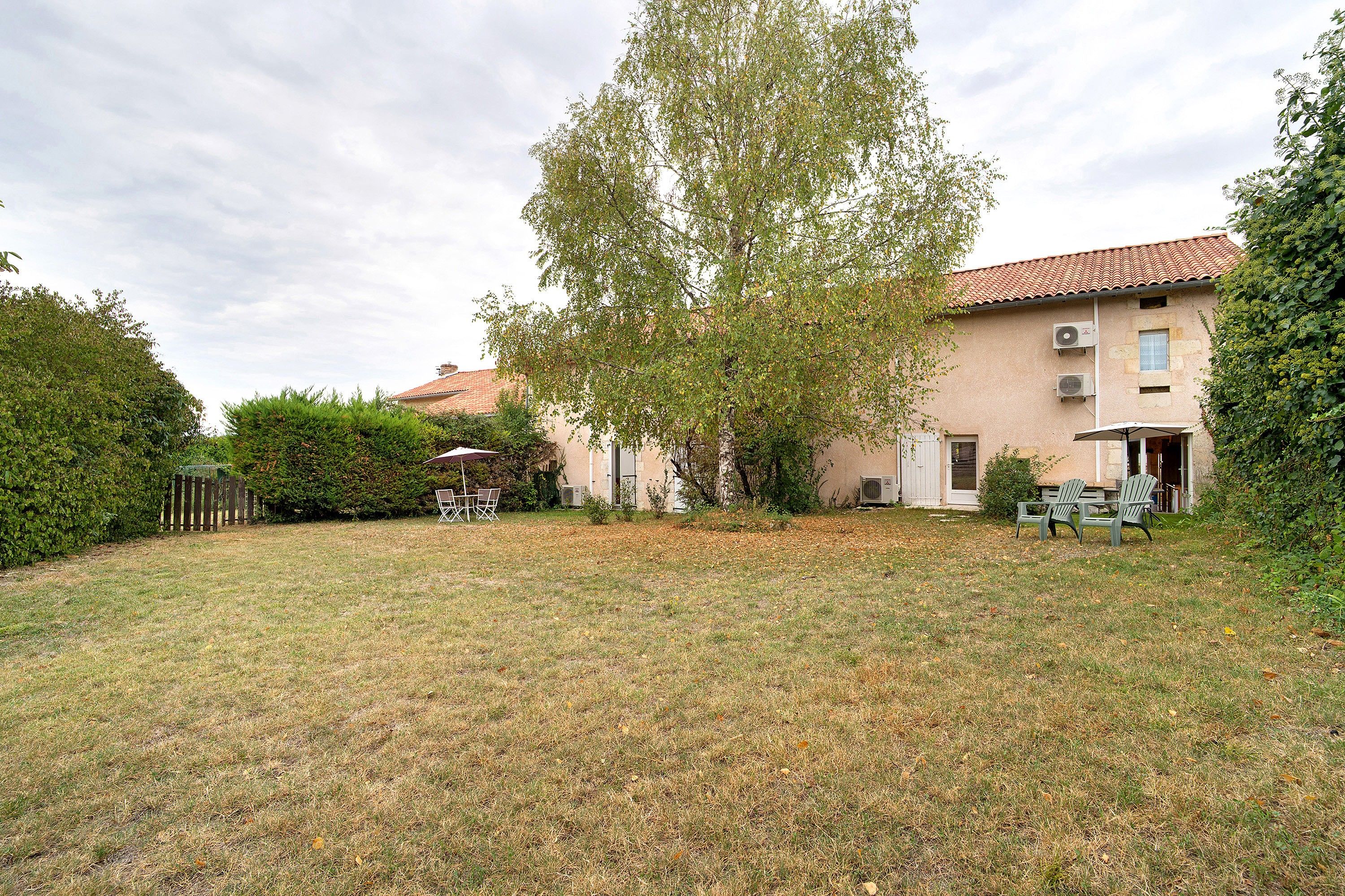 A residential property with a fenced yard, a patio with outdoor furniture, and a building with a tiled roof.