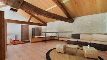 Un vaste espace de vie doté d’un plafond haut, de poutres apparentes, d’un mur en pierre, d’un ensemble de canapés, d’une table basse et d’une petite table avec des chaises.