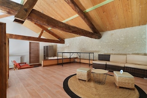 A spacious living area with a high ceiling, exposed wooden beams, a stone wall, a sofa set, a coffee table, and a small table with chairs. - Guest House 'Chambre C' with Shared Pool, Wi-Fi and Air Conditioning (Ribérac)