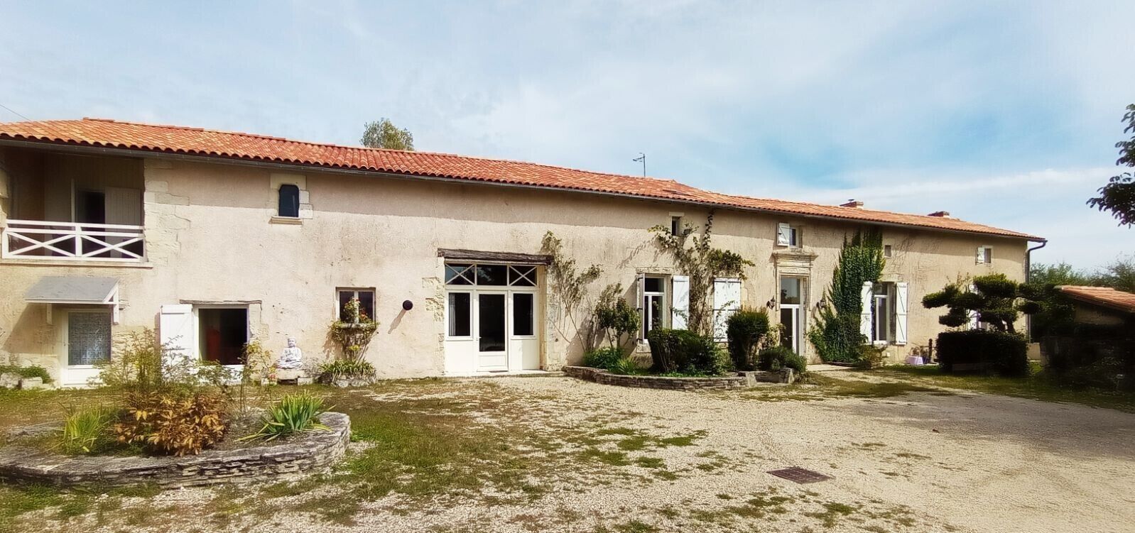 A two-story building with a red-tiled roof, multiple windows, and a gravel driveway.