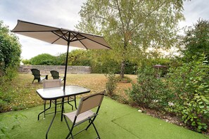 An outdoor patio with a table and chairs, a large umbrella, and a wooden fence in the background. - Guest House 'Chambre C' with Shared Pool, Wi-Fi and Air Conditioning (Ribérac)