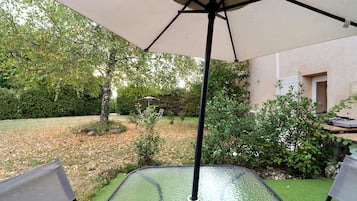 An outdoor patio area with a table and chairs, surrounded by greenery and a tree.