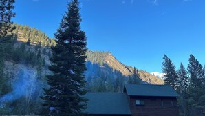A cabin with a stone foundation and a wooden exterior, surrounded by dense forest and mountains. - Rustic Big Sky "Cabin" (Superior)