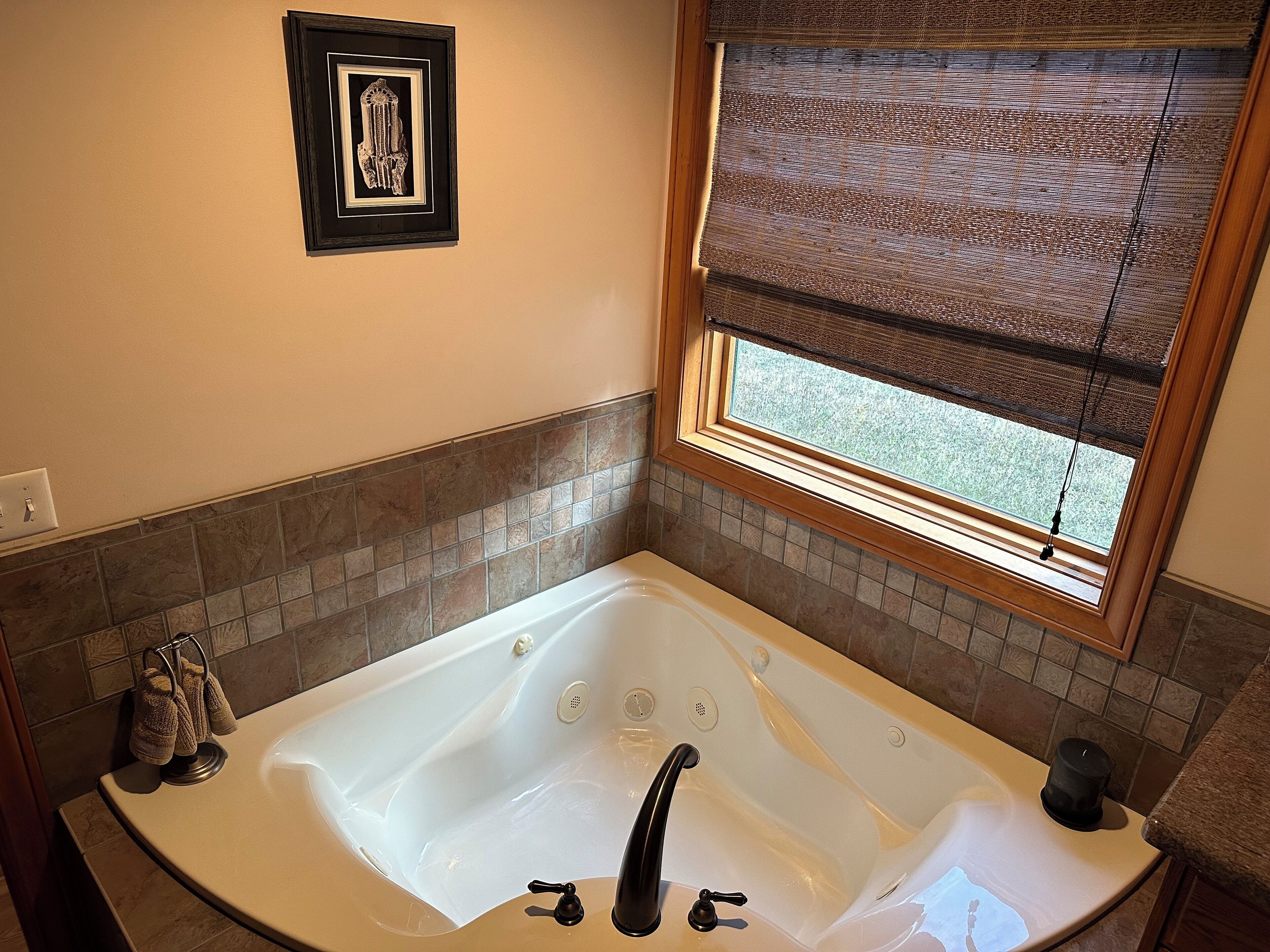 Un baño con una bañera grande, una ventana con persianas, un perchero y un cuadro enmarcado en la pared.