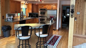 A modern kitchen with wooden cabinets, stainless steel appliances, and a bar area with two stools. - Rustic Big Sky "Cabin" (Superior)