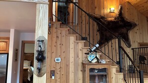 A wooden interior with a staircase, a mounted telescope, and a mounted animal head. - Rustic Big Sky "Cabin" (Superior)