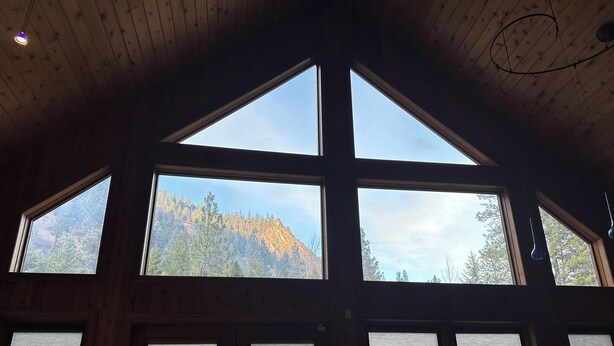 A room with large windows, wooden ceiling beams, and a view of a mountain. - Rustic Big Sky "Cabin" (Superior)