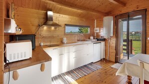 A wooden cabin interior with a kitchenette, a window with a view, and a sliding glass door leading outside. - Cottage 'Casa Da Lagoa Pateira' with Private Pool, Wi-Fi and Air Conditioning (Fermentelos)