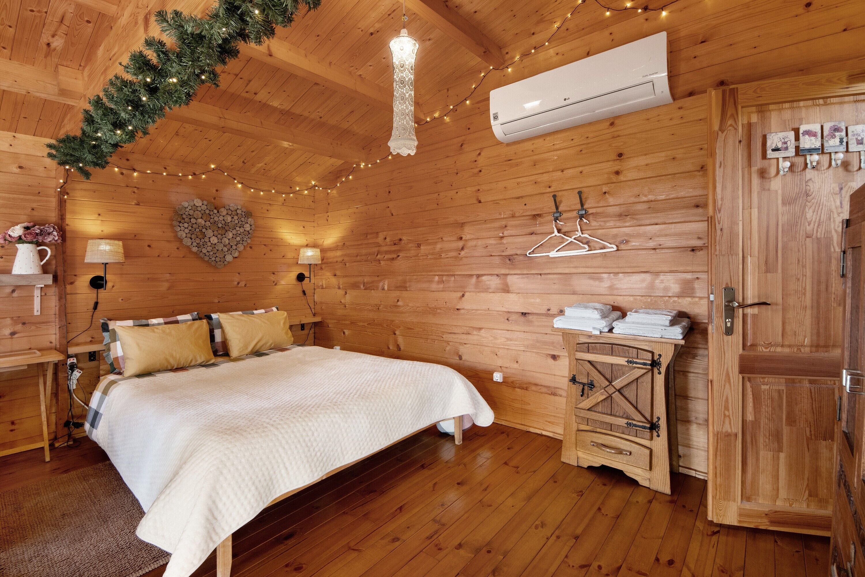 A wooden cabin bedroom with a bed, hanging lights, an air conditioner, and a wooden wardrobe.