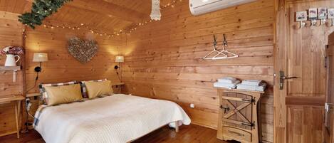 A wooden cabin bedroom with a bed, hanging lights, an air conditioner, and a wooden wardrobe.