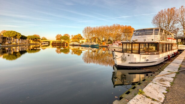 Ein ruhiger Fluss mit einem Boot am rechten Ufer, umgeben von Bäumen und Gebäuden.