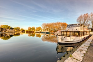 A calm river with a boat docked on the right, surrounded by trees and buildings. - Villa in the heart of the Citadel with terrace, parking, Wi-Fi and air conditioning (Aigues-Mortes)
