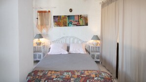 A bed with a patterned bedspread, two bedside tables with lamps, a wall with a colorful artwork, and a window with sheer curtains. - Apartment 'Duplex' with Sea View and Balcony (Grosseto-Prugna)