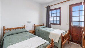 Een kamer met twee houten bedden, een raam met gordijnen, een houten deur en een wandlamp.