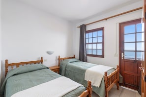 A room with two wooden beds, a window with curtains, a wooden door, and a wall-mounted light fixture. - Apartment 'Apartamento D' with Sea Views, Private Terrace and Wi-Fi (La Fajana)