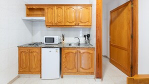 Een kleine keuken met houten kastjes, een magnetron, een spoelbak en een koelkast.