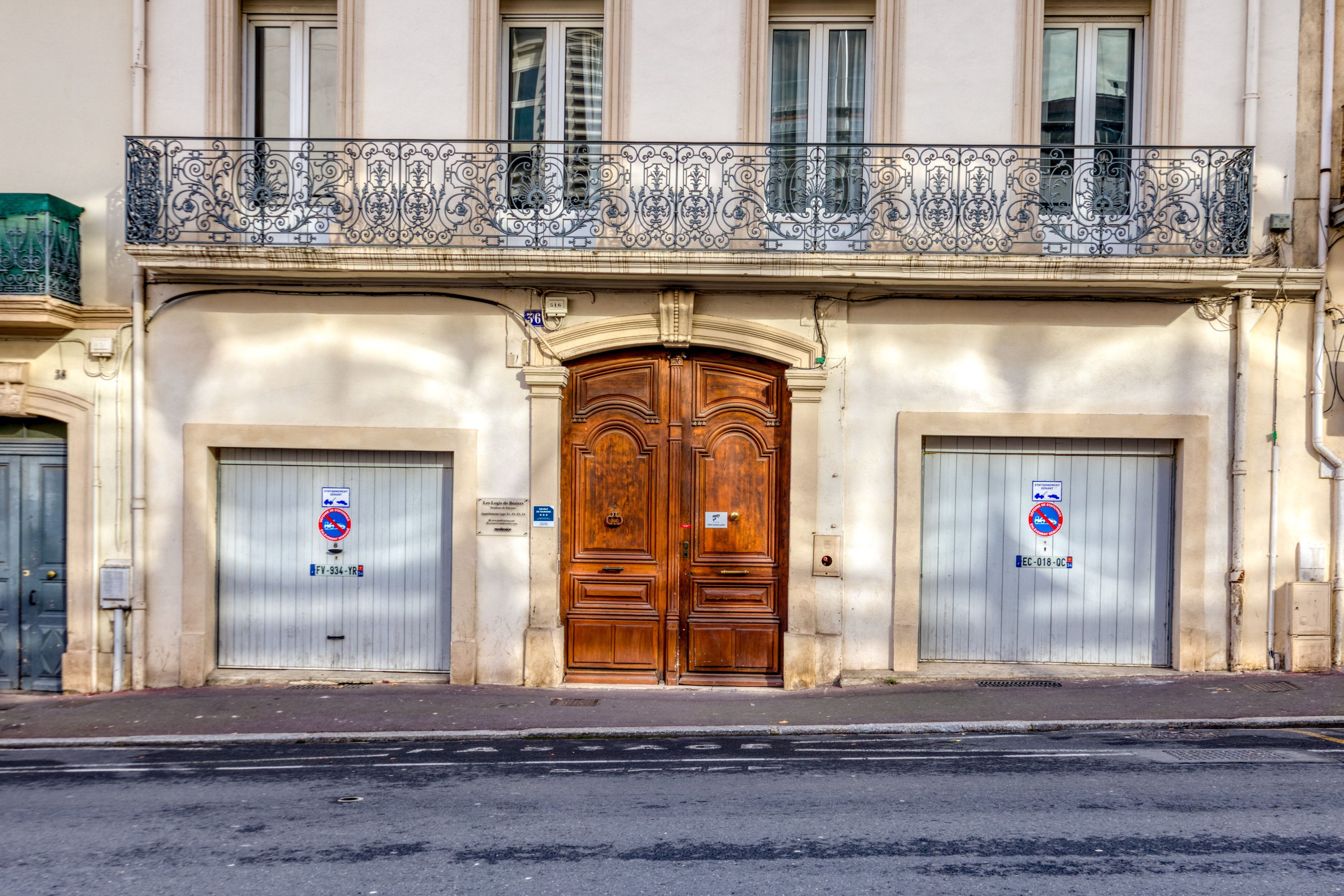 Un edificio con un'ampia porta in legno a due battenti, due piccole porte con insegne e un balcone con ringhiere in metallo finemente decorate.
