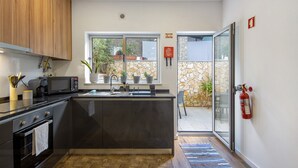 A modern kitchen with a central island, a microwave, and a stove. There is a window with a view of a stone wall and plants outside.