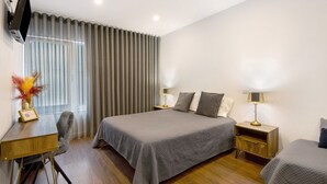 A bedroom with a large bed, two bedside tables, a desk with a chair, and a TV mounted on the wall.