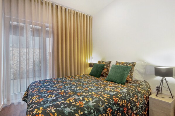 A bedroom with a large bed, a window with curtains, a bedside lamp, and a view of the outside.