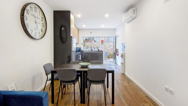 A modern kitchen with a dining area, a clock, and a view to the outside.