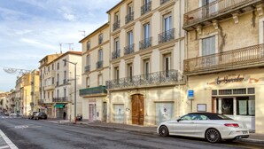 A street with multi-story buildings, a white car parked on the side, and a shop with a sign.