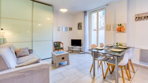 A modern living room with a sofa, a dining table with chairs, a TV, and a glass partition.