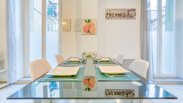 A modern dining area with a glass table, white chairs, and a cityscape view through the glass doors.