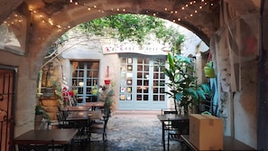 An outdoor café with tables and chairs, a blue door with glass panels, and string lights.