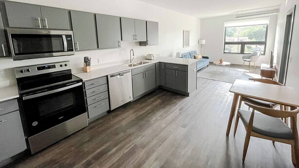 Una cocina moderna con armarios grises, electrodomésticos de acero inoxidable y una mesa de comedor de madera.