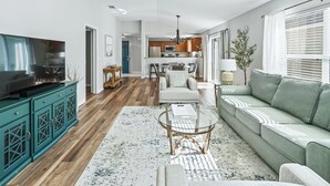 A spacious living room with a large TV, a sofa, a coffee table, and a dining area in the background. - Long term pricing - Charming 2 bed Villa awaits for you. (The Villages)