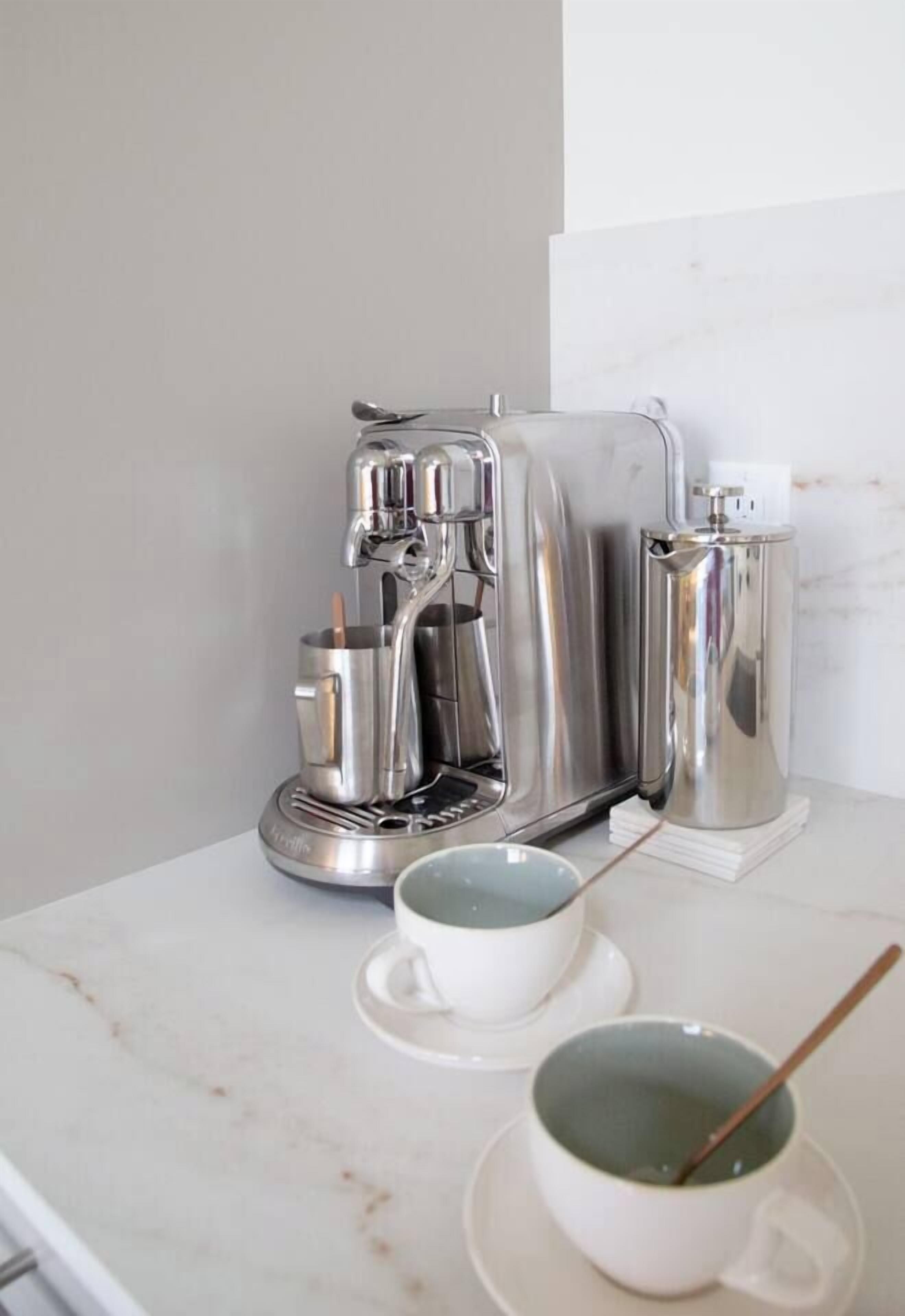Uma cozinha com cafeteira, chaleira e duas chávenas sobre uma bancada de mármore.