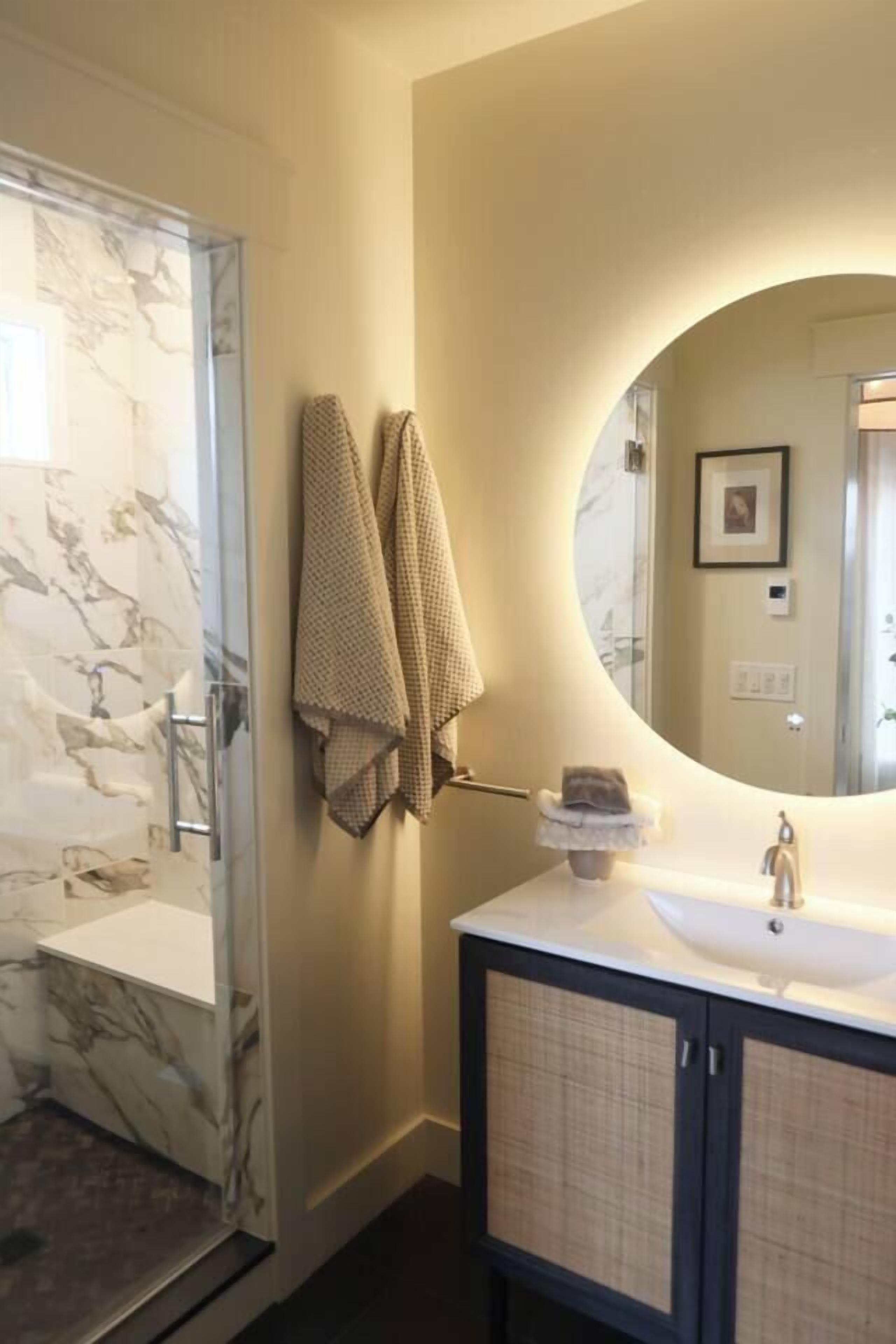 A bathroom with a marble shower, a sink with a mirror, and two towels hanging on the wall.