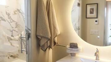 A bathroom with a marble shower, a sink with a mirror, and two towels hanging on the wall.