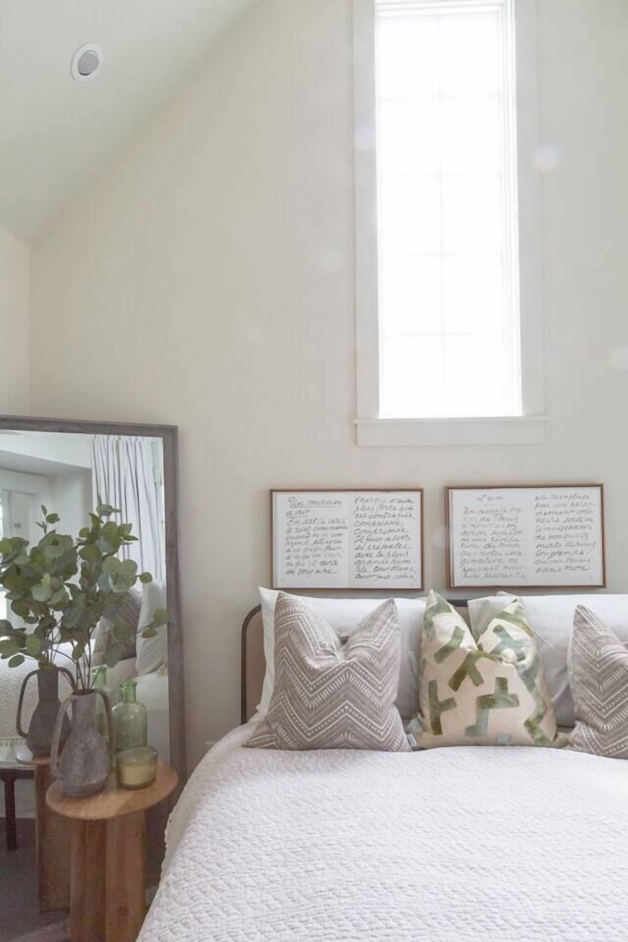 Ein Schlafzimmer mit einem großen Bett, einem Spiegel, einem Fenster und zwei gerahmten Texttafeln an der Wand.