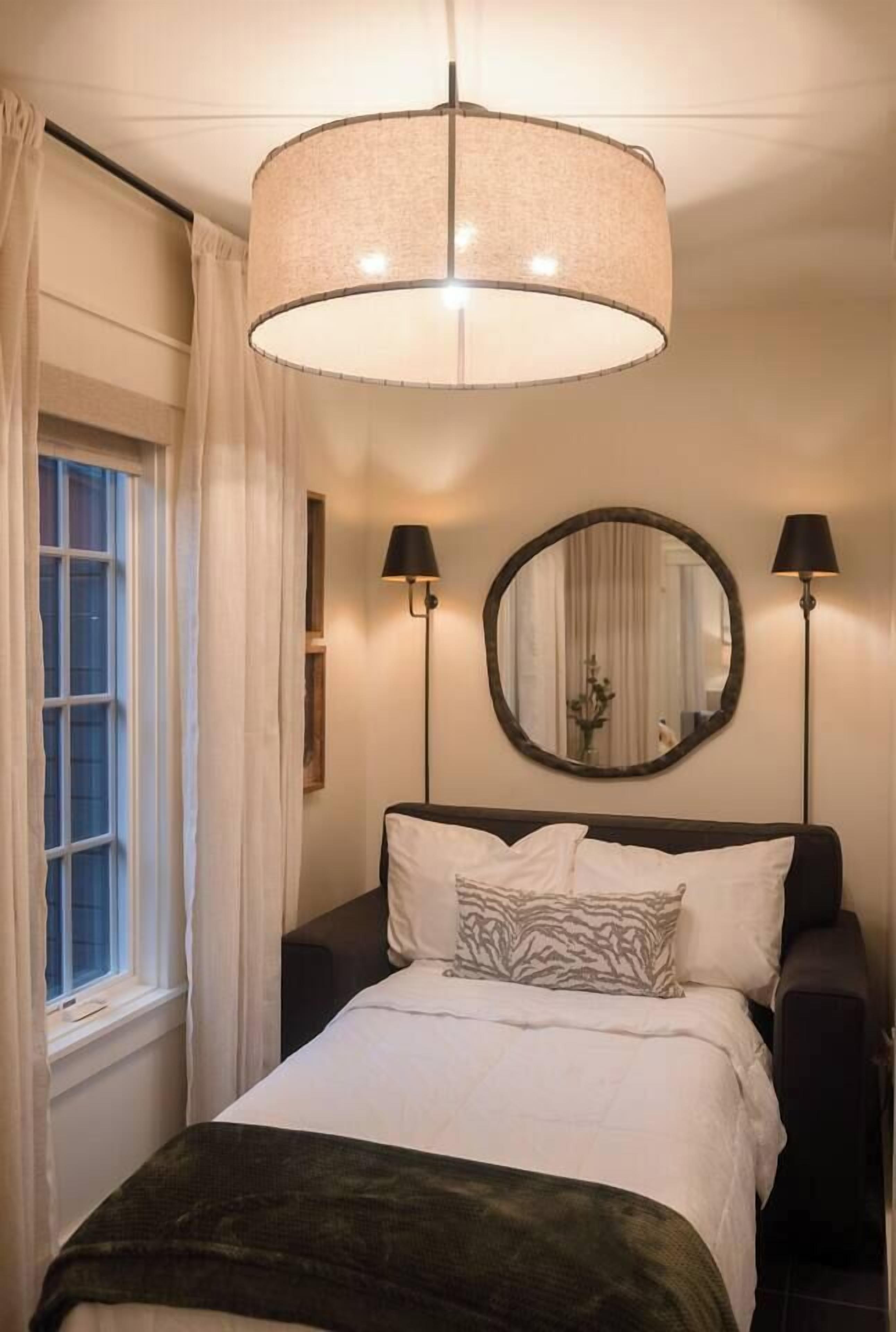 Une chambre à coucher avec un lit, un miroir rond, deux lampes de chevet et une fenêtre avec des rideaux.